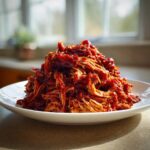A generous mound of saucy, shredded pulled chicken piled high on a white plate, ready to serve.