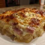 A close-up of a square serving of cheesy scalloped potatoes and ham with a golden-brown, bubbly top.