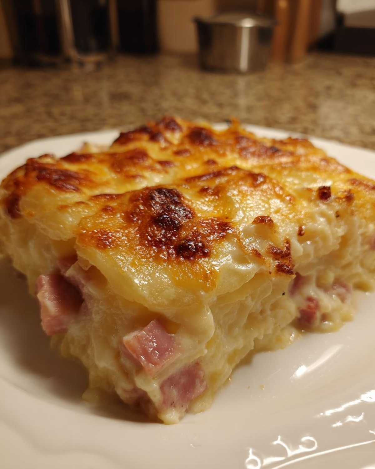 A close-up of a hearty slice of scalloped potatoes and ham with a golden, bubbly cheese crust.