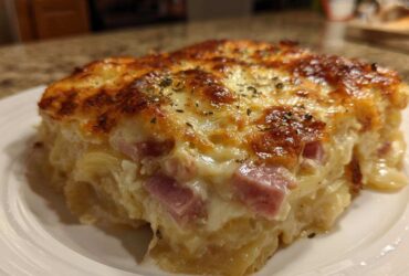 A close-up of a square serving of cheesy scalloped potatoes and ham with a golden-brown, bubbly top.