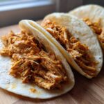 Close-up of three soft tortillas filled generously with seasoned, shredded chicken for amazing chicken tacos.