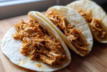 Close-up of three soft tortillas filled generously with seasoned, shredded chicken for amazing chicken tacos.