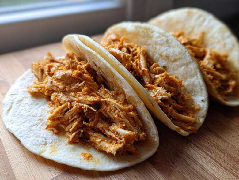 Close-up of three soft tortillas filled generously with seasoned, shredded chicken for amazing chicken tacos.