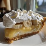 A perfect slice of banana cream pie recipe featuring a graham cracker crust, creamy filling, sliced bananas, and a generous topping of whipped cream.
