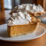 A close-up of a thick slice of creamy butterscotch pie topped generously with whipped cream.