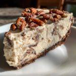 A close-up slice of silky pecan cream pie featuring a thick, creamy filling studded with pecans and topped with whole toasted pecans.