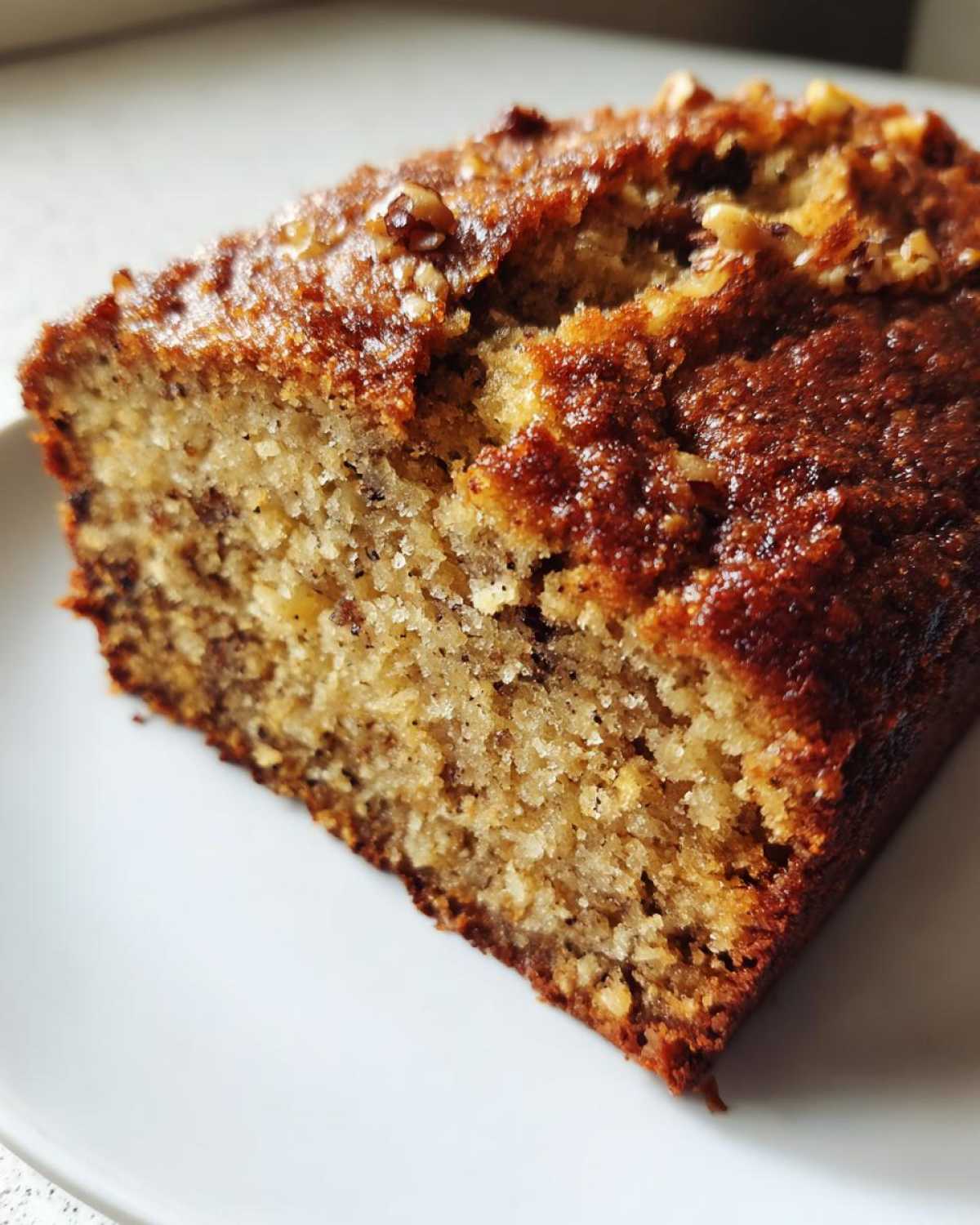 Close-up of a moist slice of sugar free banana bread showing a rich, caramelized top and visible walnuts.