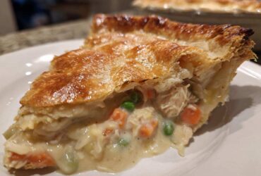 Close-up of a slice of turkey pot pie showing creamy filling, turkey, carrots, and peas under a golden, flaky crust.