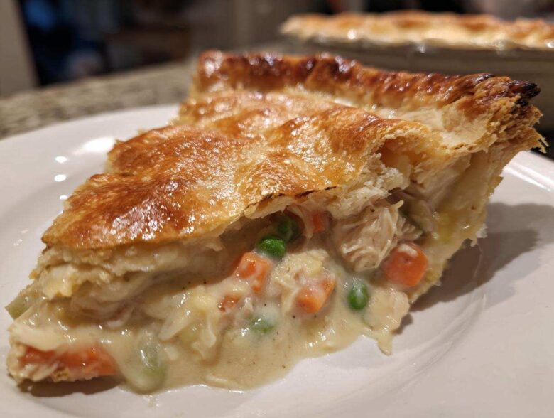 Close-up of a slice of turkey pot pie showing creamy filling, turkey, carrots, and peas under a golden, flaky crust.