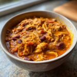 Close-up of a hearty bowl of slow cooker buffalo chicken chili, featuring shredded chicken and kidney beans in a rich, orange sauce.