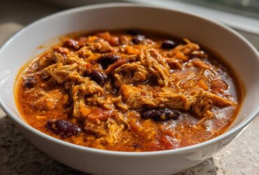 A close-up view of a hearty bowl of slow cooker buffalo chicken chili, featuring shredded chicken and kidney beans in a rich, orange-red sauce.