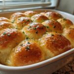A close-up of twelve golden brown, soft buttery garlic rolls soaking in melted butter and topped with parsley.
