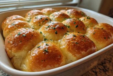 A close-up of twelve golden brown, soft buttery garlic rolls soaking in melted butter and topped with parsley.