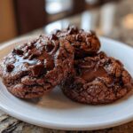 Three rich, dark chocolate pudding cookies with pools of melted chocolate chips on a white plate.