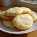 A stack of five soft sugar cookies with a slightly crackled top, resting on a white plate bathed in natural sunlight.