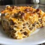 A close-up of a hearty slice of sour cream beef noodle casserole topped with melted, browned cheddar cheese.