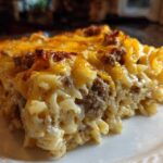 A close-up of a hearty slice of sour cream beef noodle casserole topped with melted, browned cheddar cheese.