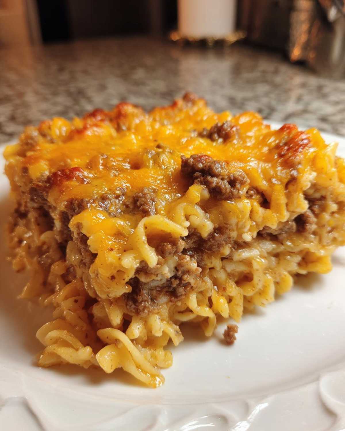 A close-up serving of sour cream beef noodle casserole topped with melted, browned cheddar cheese.