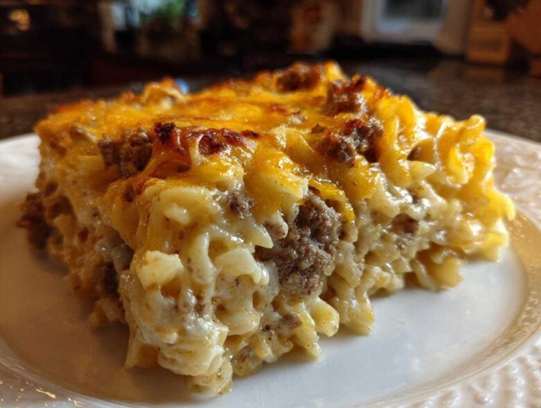 A close-up of a hearty slice of sour cream beef noodle casserole topped with melted, browned cheddar cheese.