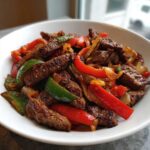 Close-up of perfectly cooked steak fajitas featuring strips of seasoned steak, red bell peppers, green peppers, and onions in a white bowl.