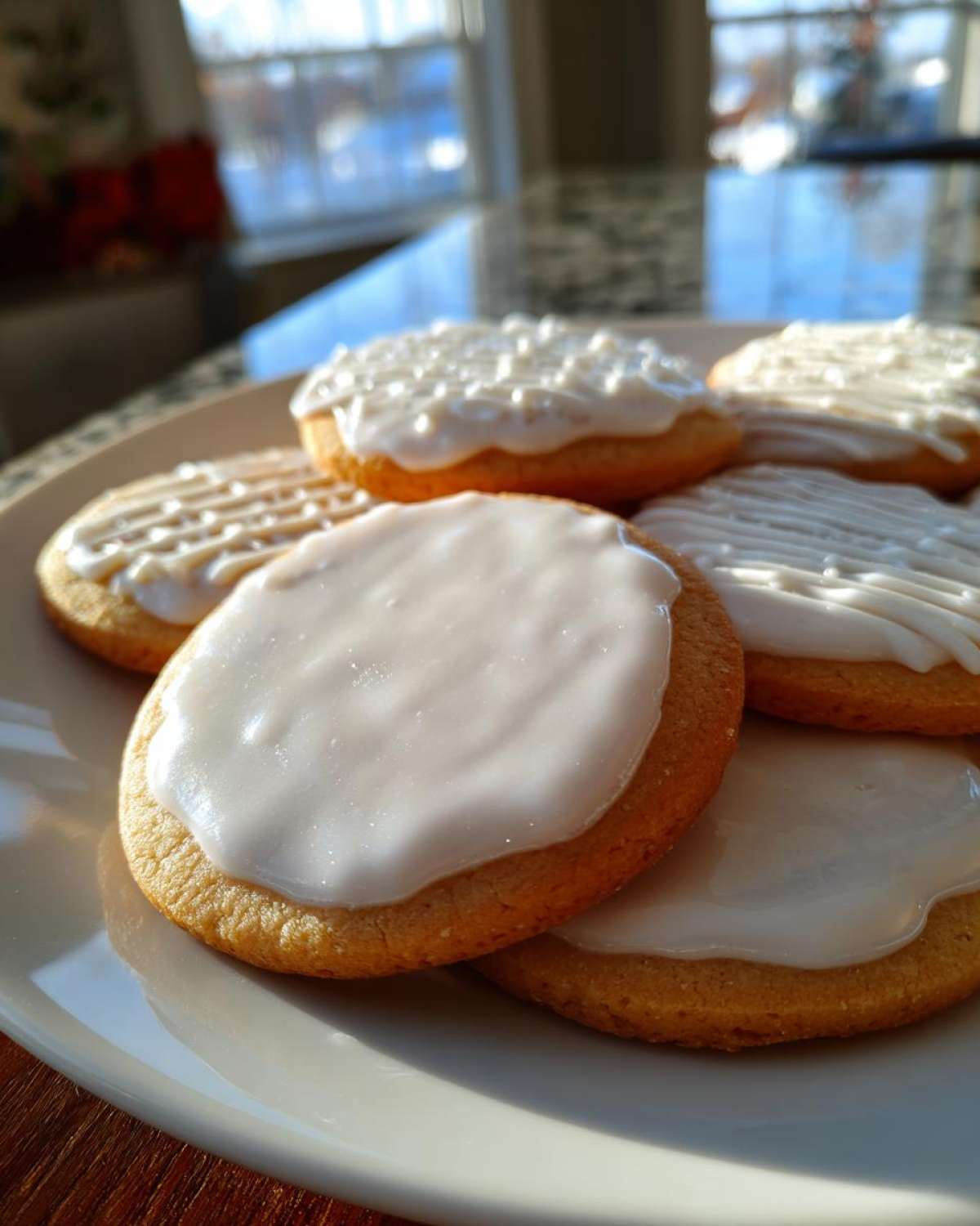 Close-up of round sugar cookies topped with thick, glossy white cookie icing recipe glaze on a white plate.