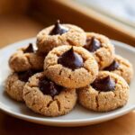 A stack of freshly baked peanut butter blossom cookies, rolled in sugar and topped with a chocolate kiss.