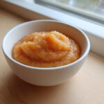 A close-up of homemade applesauce with a slightly chunky texture served in a small white bowl.