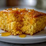Close-up of a moist, golden slice of sweet potato cornbread topped with dripping honey on a white plate.