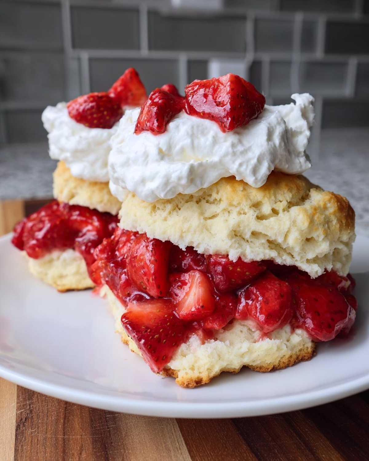 Close-up of a tender shortcake split open, filled with macerated strawberries and topped with whipped cream.