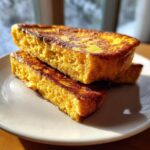 Close-up of two thick slices of golden brown french toast stacked on a white plate.