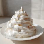 A tall, perfectly piped swirl of creamy white vanilla buttercream frosting sitting on a small white plate.