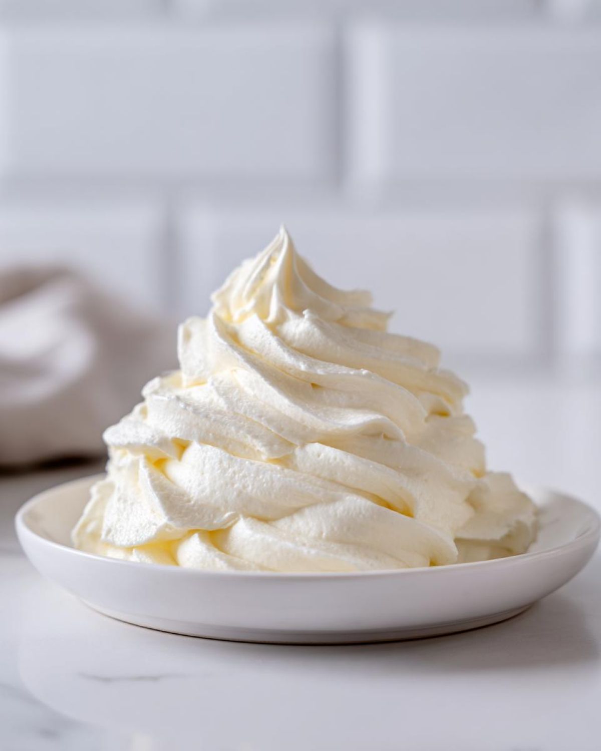 A tall, perfectly piped swirl of creamy vanilla buttercream frosting served in a small white bowl.