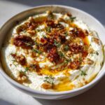 A creamy bowl of whipped ricotta dip with hot honey, walnuts, and fresh thyme garnish.