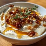 Close-up of a creamy whipped ricotta dip with hot honey, candied walnuts, and a sprig of thyme.
