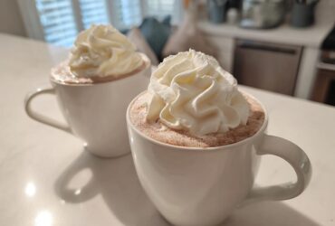 Two white mugs filled with rich white hot chocolate topped generously with swirls of whipped cream.