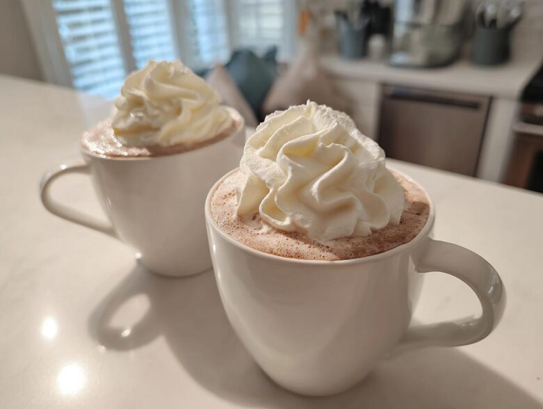 Two white mugs filled with rich white hot chocolate topped generously with swirls of whipped cream.