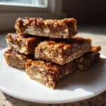 A stack of homemade, chewy, nut-filled protein bars glistening under natural light.