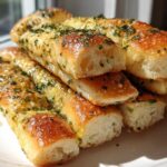 A stack of golden, soft breadsticks brushed with garlic butter and sprinkled with parsley.