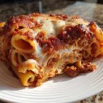 Close-up of a hearty slice of baked ziti style pasta bake, showing layers of rigatoni, meat sauce, and melted cheese.