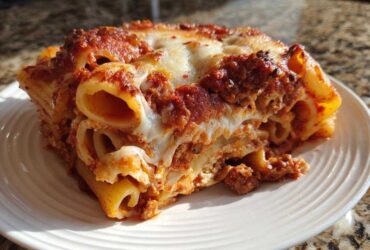 Close-up of a hearty slice of baked ziti style pasta bake, showing layers of rigatoni, meat sauce, and melted cheese.