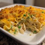A close-up view of a creamy, cheesy Tuna Casserole topped with golden breadcrumbs and green peas.