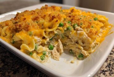 A close-up view of a creamy, cheesy Tuna Casserole topped with golden breadcrumbs and green peas.