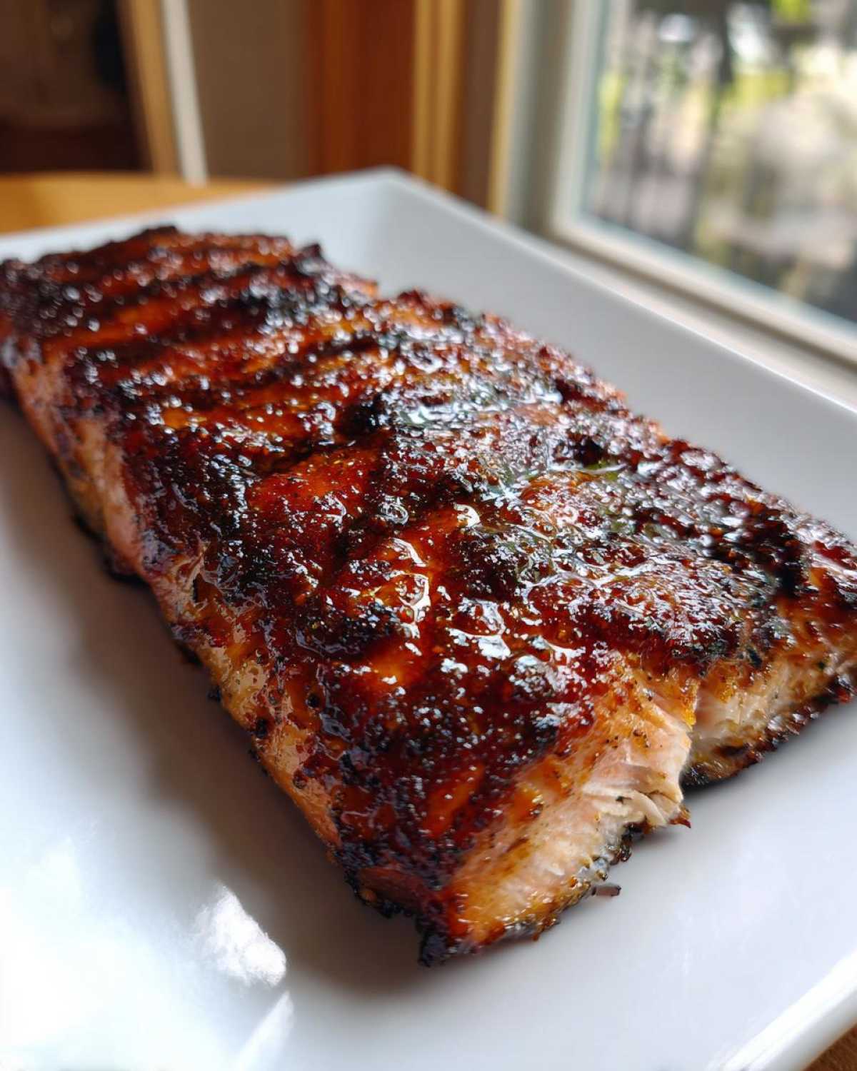 Close-up of a perfectly cooked salmon fillet with a dark, shiny, caramelized glaze served on a white rectangular plate.