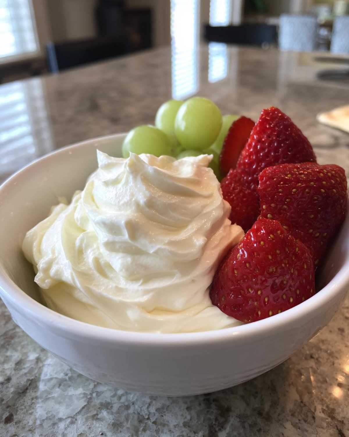A white bowl filled with creamy fruit dip, fresh strawberries, and green grapes, perfect for dipping.