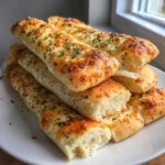 A stack of freshly baked, cheesy garlic breadsticks topped with herbs, ready to eat.