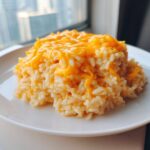 A mound of creamy cheesy rice topped with melted bright orange cheddar cheese.