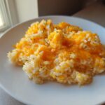 A serving of amazing cheesy rice topped with bright orange melted cheddar cheese on a white plate.