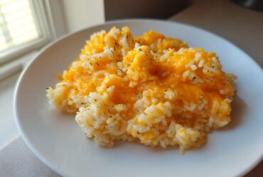 A serving of amazing cheesy rice topped with bright orange melted cheddar cheese on a white plate.