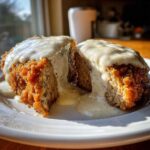 Cross-section of a golden brown chicken fried steak smothered in creamy white peppered gravy.