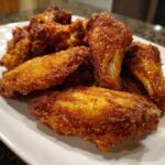 A close-up shot of several golden-brown, crispy chicken wings piled on a white plate.